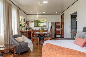 Ein modernes Hotelzimmer mit Bett, Sofa, Esstisch mit Stühlen, Küchenzeile und Bad.