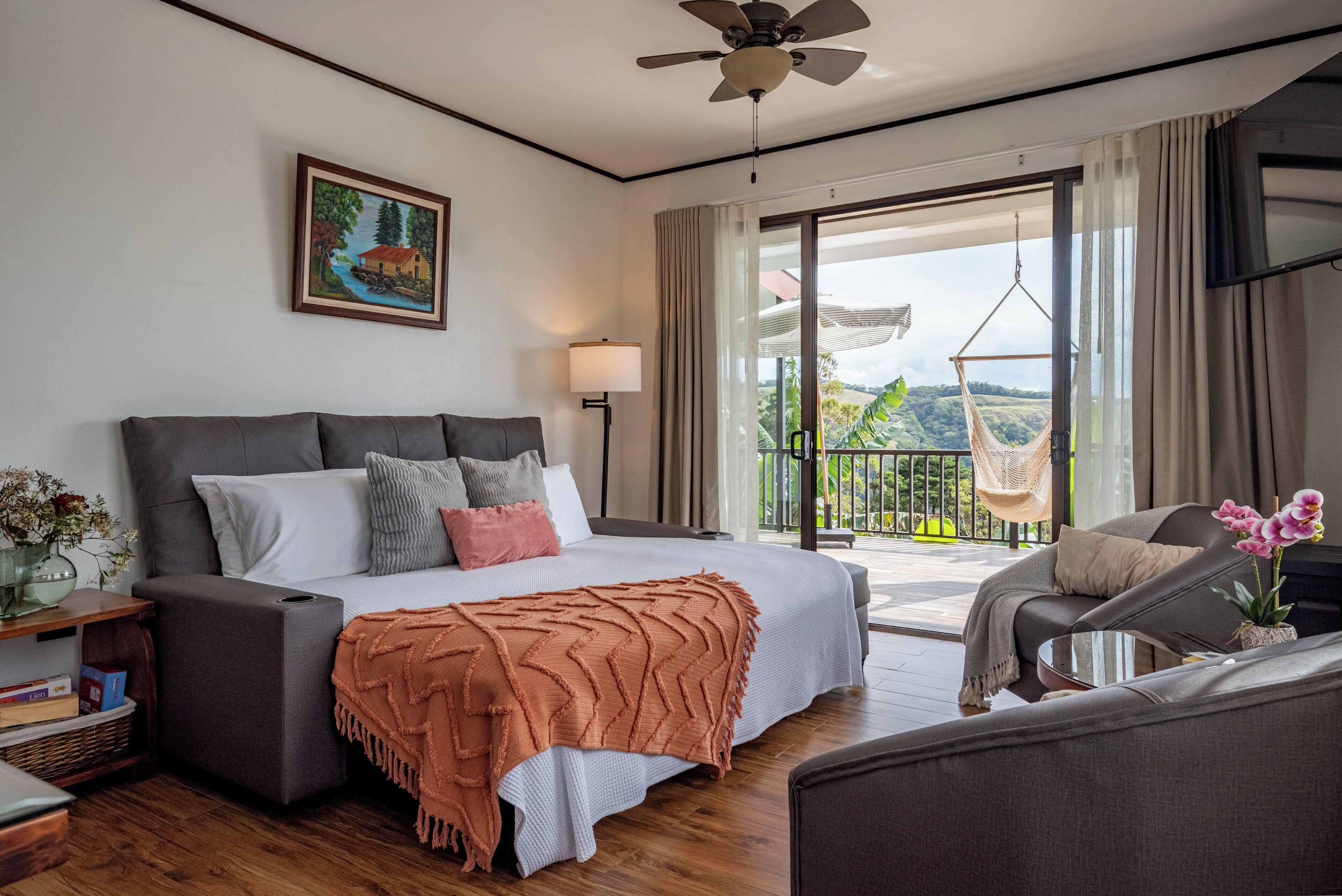 Un dormitorio con cama, mesita de noche, lámpara y vistas al exterior.