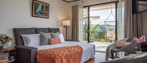 A bedroom with a bed, bedside table, lamp, and a view of the outdoors.