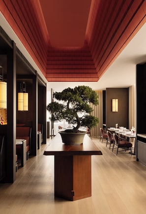 A modern interior with a central wooden table, a bonsai tree, and a dining area with chairs and tables. - Capella Taipei (Taipei)
