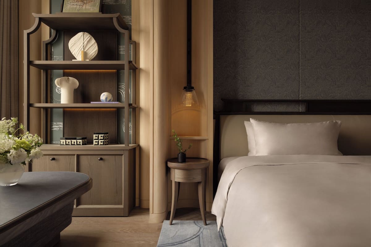 A modern bedroom with a large bed, a nightstand, a bookshelf, and a small table with a plant.