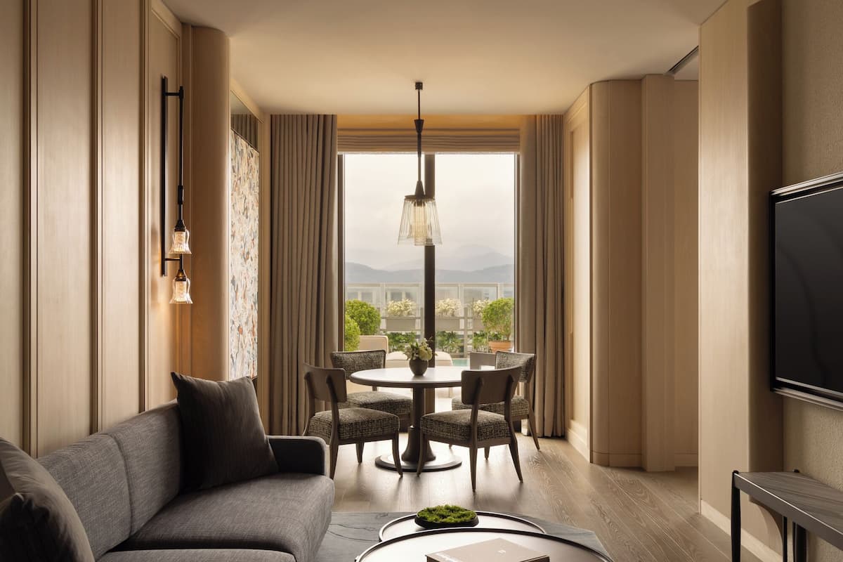 A modern hotel room with a sofa, dining table, chairs, and a TV.