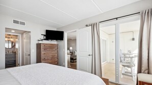 Et soveværelse med en stor seng, en trækommode, et fjernsyn og en skydedør til en balkon med et bord og stole.