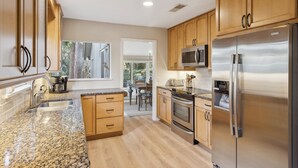 A modern kitchen with wooden cabinets, stainless steel appliances, granite countertops, and a view to the outside. - Relax in Sea Pines | Bikes to Beach, Golf & Family Fun Included (Hilton Head Island)