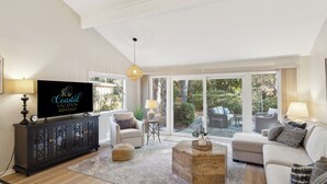 A spacious living room with a large television, comfortable seating, and a view of the outdoors through large sliding glass doors. - Relax in Sea Pines | Bikes to Beach, Golf & Family Fun Included (Hilton Head Island)