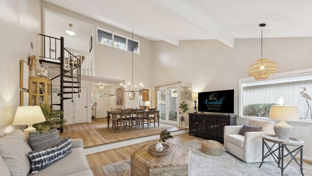 A spacious living room with a high ceiling, a staircase, a dining area, and a television. - Relax in Sea Pines | Bikes to Beach, Golf & Family Fun Included (Hilton Head Island)