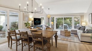 A spacious living room with a wooden dining table, comfortable seating, and large windows offering a view of the outdoors. - Relax in Sea Pines | Bikes to Beach, Golf & Family Fun Included (Hilton Head Island)