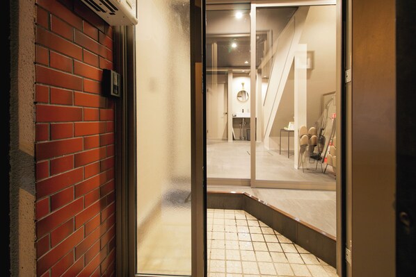 An interior view of a hotel lobby with a red brick wall, a glass door, and a tiled floor.