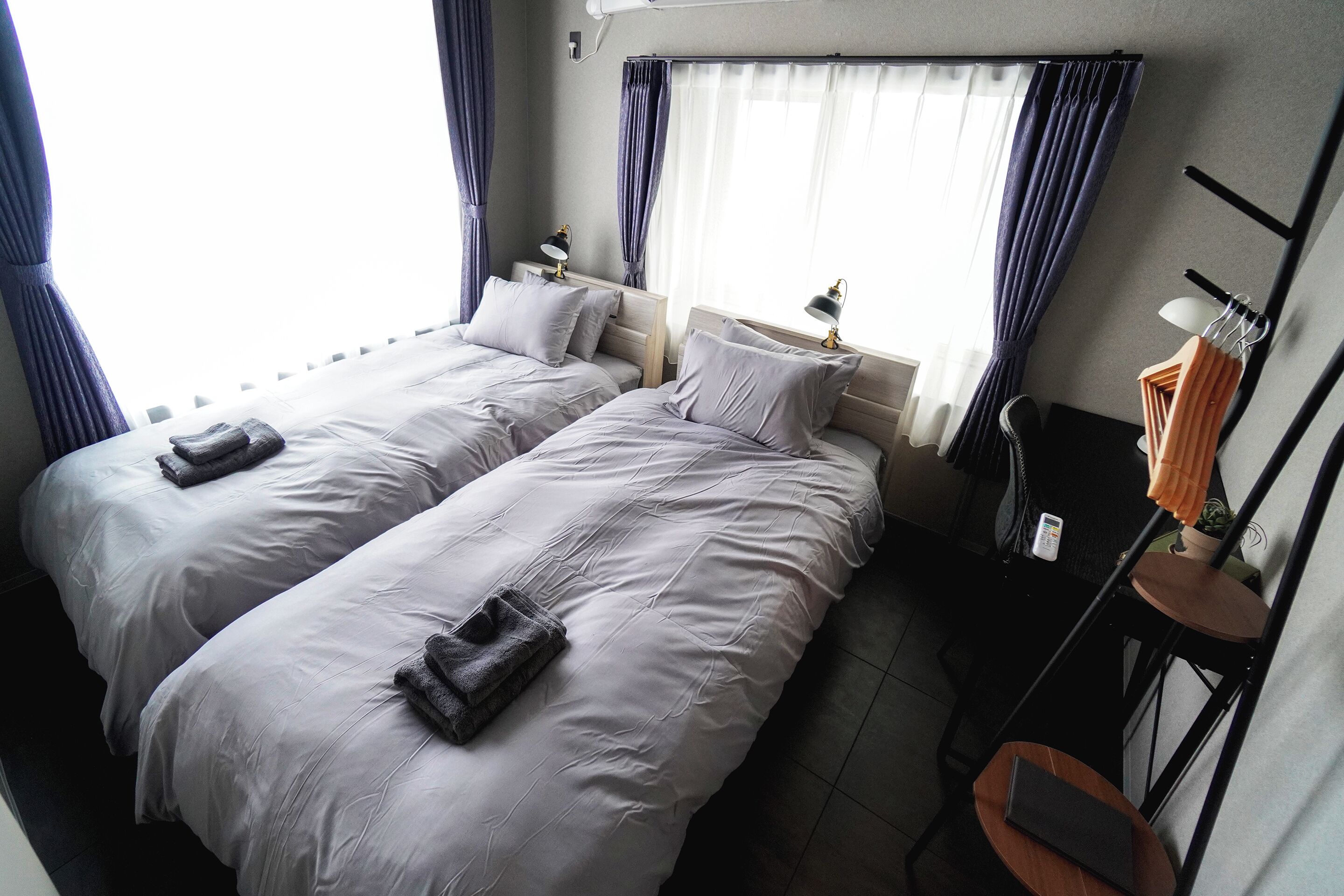 A hotel room with two beds, a small desk, a chair, and a window with curtains.