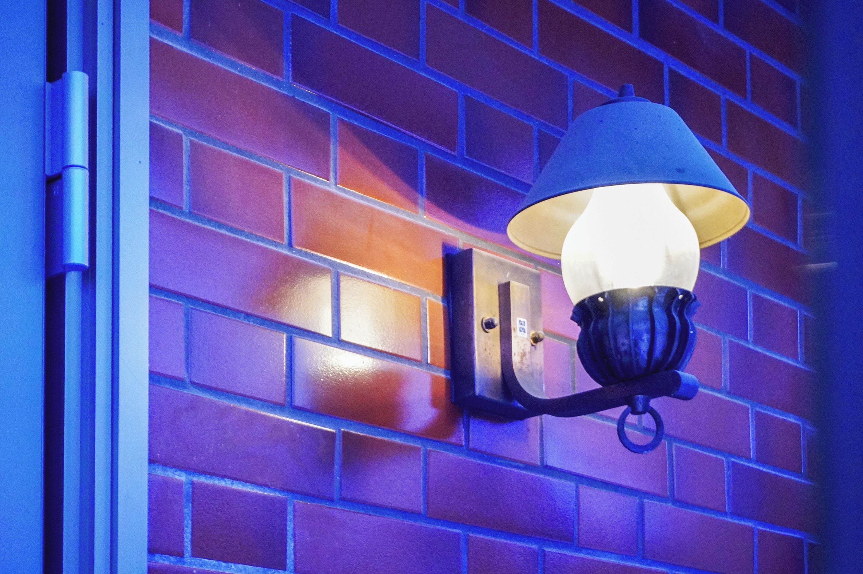 A wall-mounted outdoor light fixture with a conical shade, attached to a brick wall.