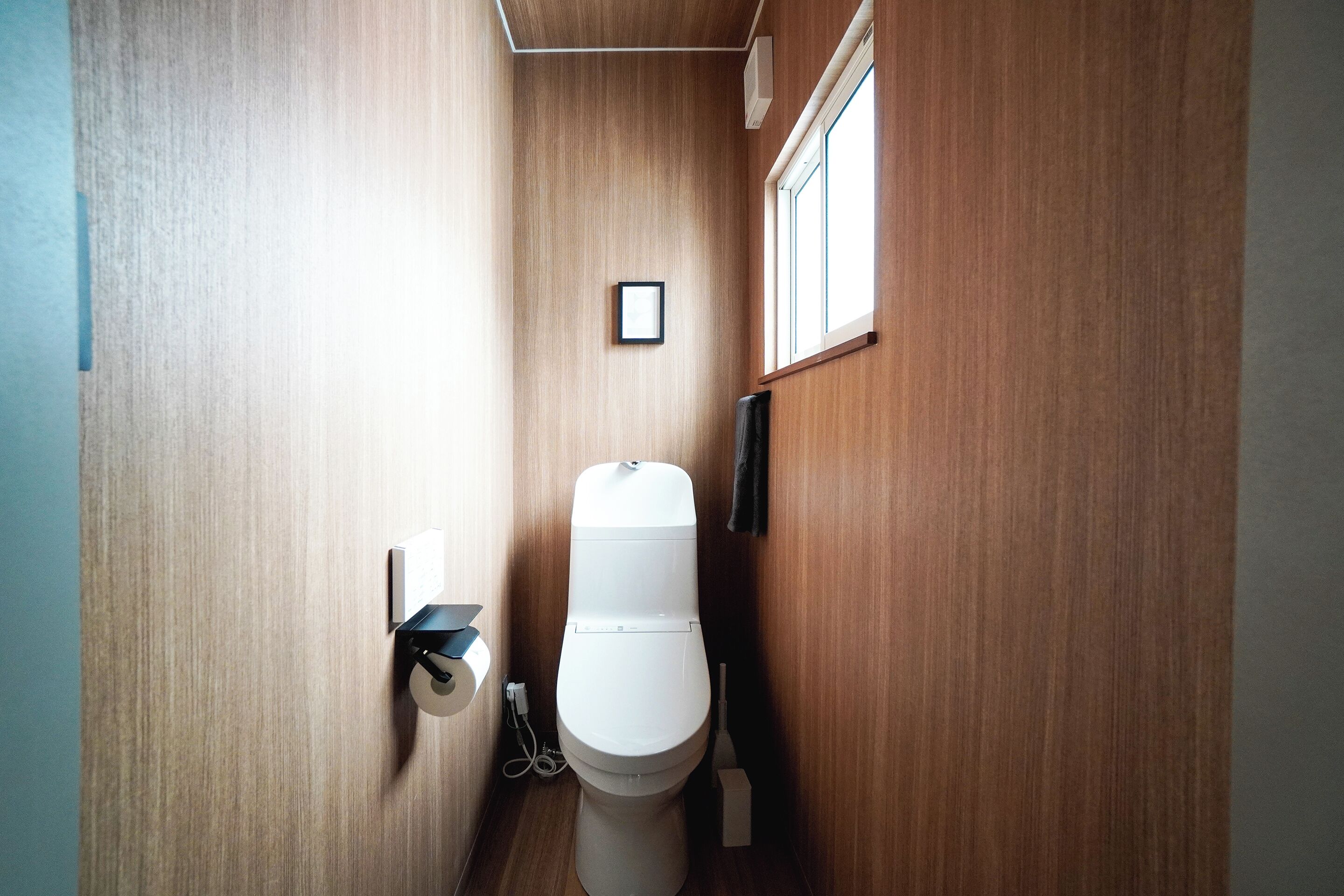 Une petite salle de bain étroite aux murs en bois, avec des toilettes blanches, une petite fenêtre et un tableau accroché au mur.