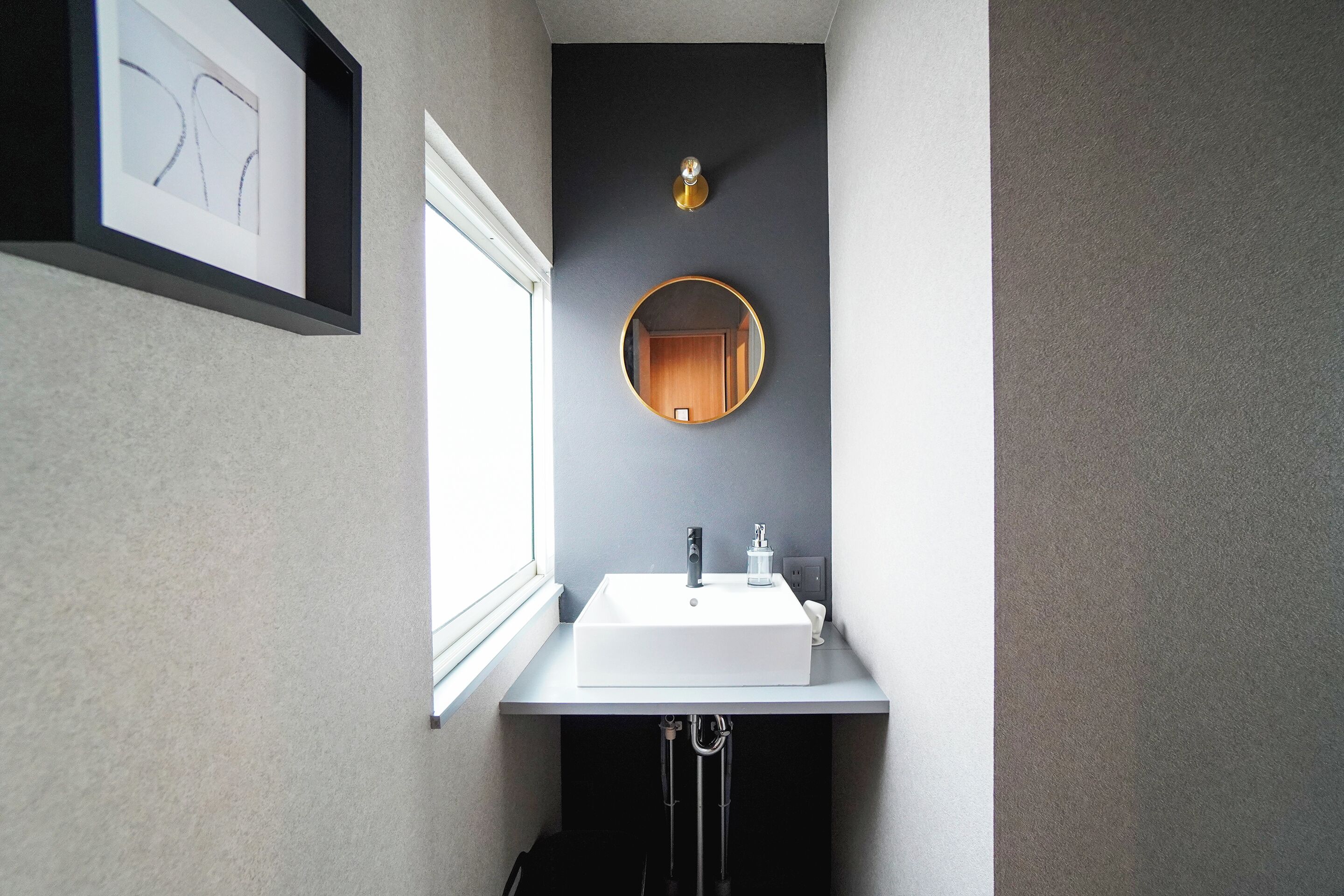 A modern bathroom with a white sink, a round mirror, and a framed artwork on the wall.