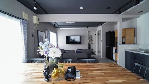A modern living room with a wooden floor, a grey sofa, a flat-screen TV, and a kitchen area with dark cabinets.