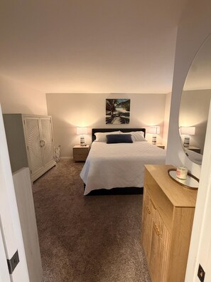 Ein Schlafzimmer mit Bett, Nachttischlampen, einem Kleiderschrank, einem Bild an der Wand und einem Spiegel.