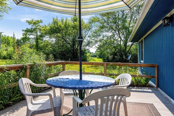 A patio with a round table and four chairs, a striped umbrella, and a wooden deck railing.
