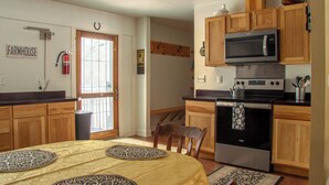 A kitchen with wooden cabinets, a microwave, an oven, and a dining area with a table and chairs. - Spacious 4BR Fennville Farmhouse w/ Pool Table (Fennville)