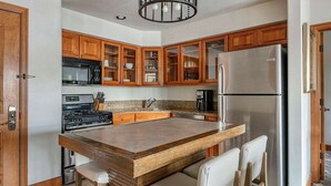 Eine Küche mit Holzausstattung, einem Edelstahlkühlschrank, einer integrierten Kochinsel mit Barhocker und einem Gasherd.
