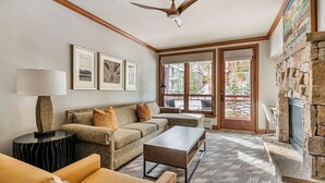 Ein Wohnzimmer mit einer Couch, einem Couchtisch und einem Kamin. An den Wänden hängen Bilder in Rahmen, und es gibt einen Deckenventilator.