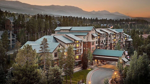 Ein mehrstöckiges Hotel mit Gründach, umgeben von Bäumen und Bergen im Hintergrund.