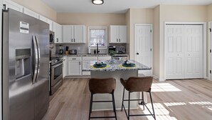 Una cocina moderna con armarios blancos, electrodomésticos de acero inoxidable y una isla central con dos taburetes de bar.