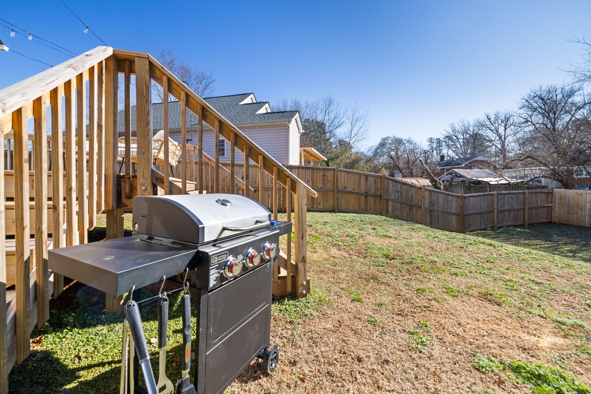 A backyard with a wooden deck, a barbecue grill, and a house in the background.