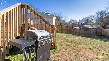A backyard with a wooden deck, a barbecue grill, and a house in the background.