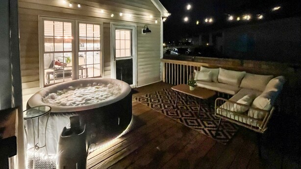 Un jacuzzi en una terraza de madera con un sofá blanco y una alfombra estampada.