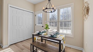 Un comedor con una mesa de madera preparada para cuatro personas, un candelabro y una ventana con persianas.