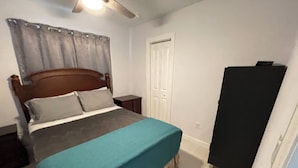 Un dormitorio con cama, mesita de noche, armario y ventilador de techo.