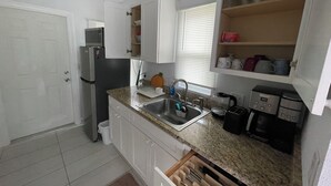 Cocina compacta con armarios blancos, un refrigerador de acero inoxidable, microondas, lavamanos con grifo, cafetera y tostadora.