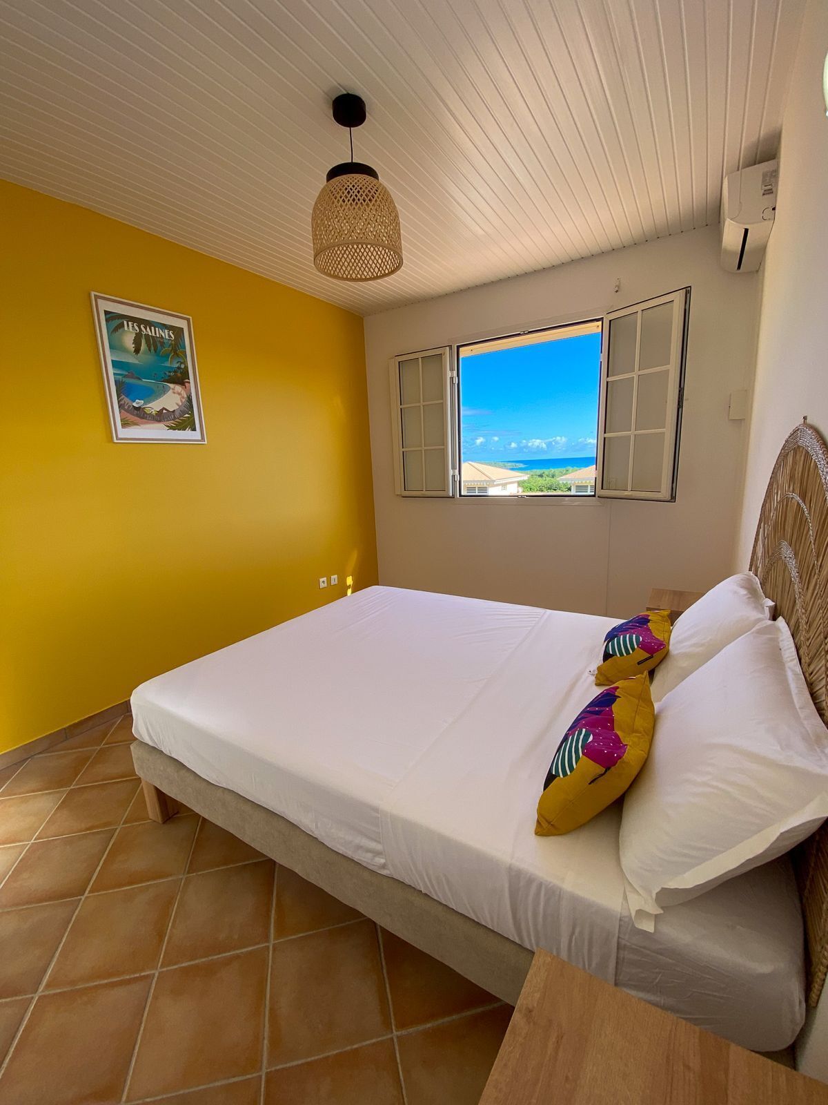 Une chambre à coucher avec un lit, une fenêtre donnant sur un beau paysage, un luminaire suspendu et une affiche accrochée au mur.