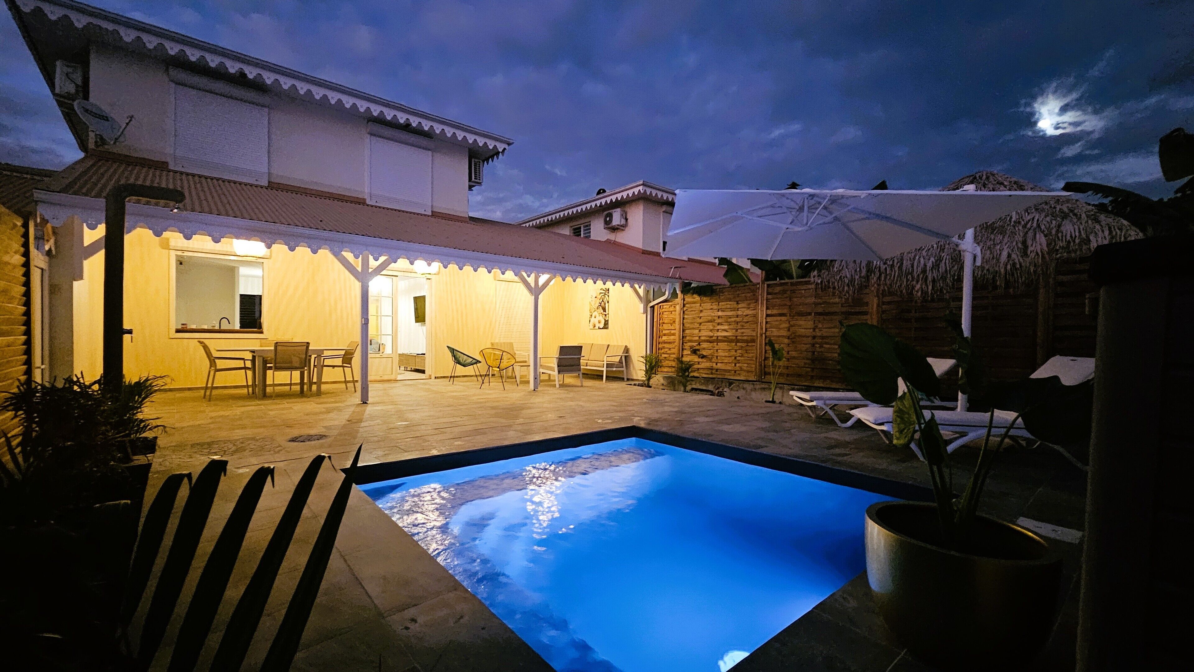 Un espace piscine doté d’un patio couvert, de chaises longues et d’un coin repas.