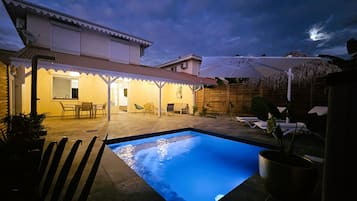 Un espace piscine doté d’un patio couvert, de chaises longues et d’un coin repas.