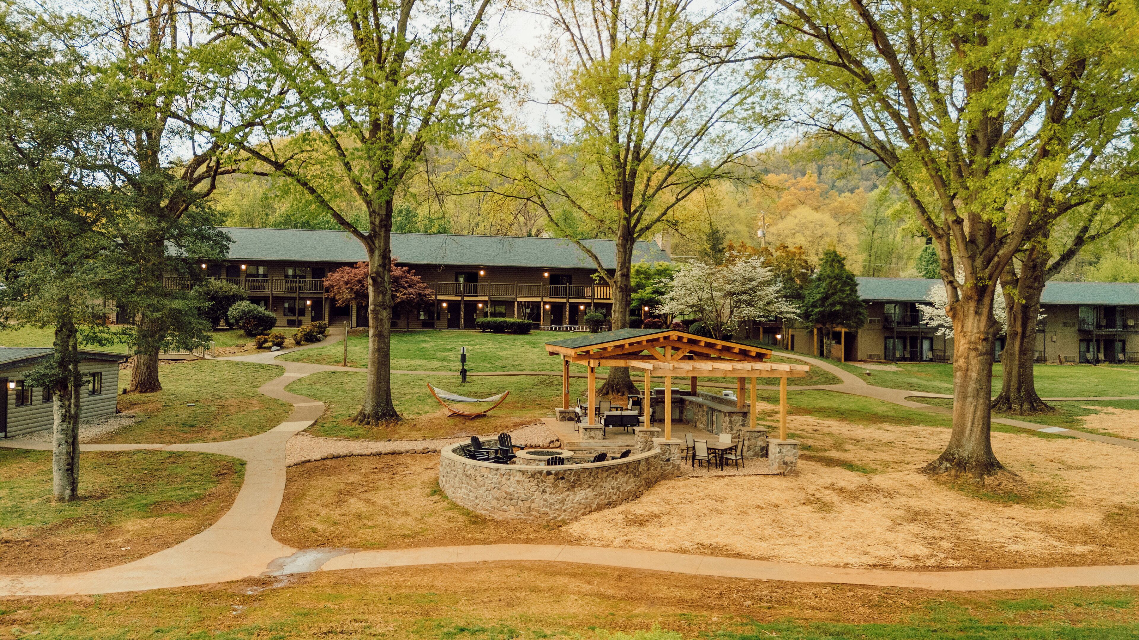 A lodge with a covered outdoor seating area, a stone fire pit, and a winding path.
