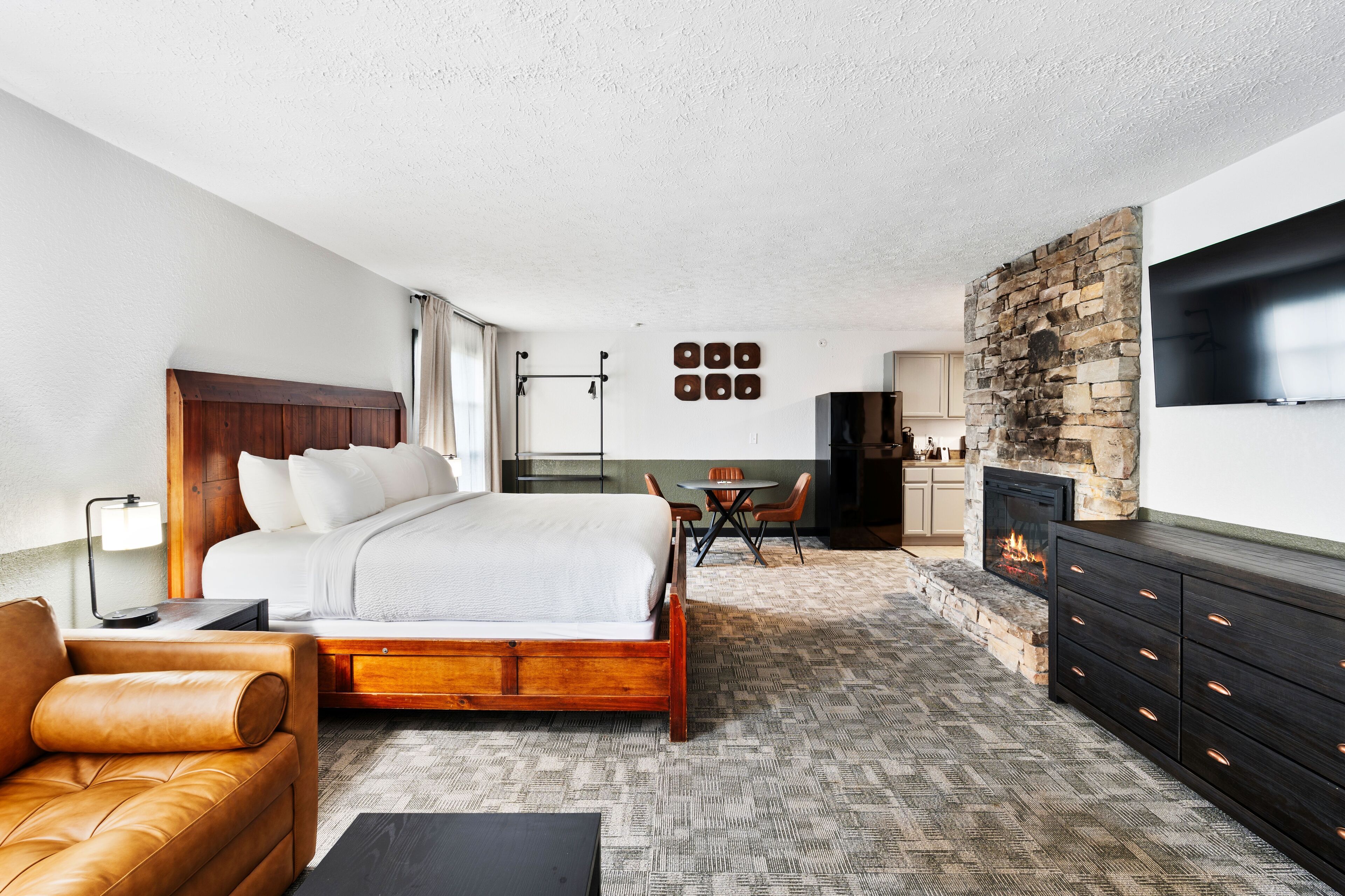 A hotel room with a bed, a sofa, a TV, a fireplace, and a stone wall.