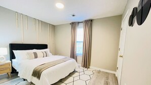 Un dormitorio con una cama grande, una mesita de noche, una ventana con cortinas y una alfombra de diseño geométrico.