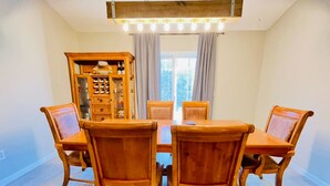 Un comedor con mesa y sillas de madera, un armario con botellas de vino y una ventana con cortinas.