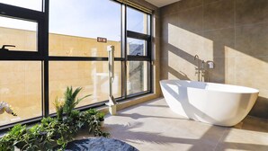 Un baño moderno con una bañera independiente, ventanas amplias y plantas en macetas.