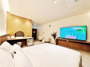 Una habitación de hotel moderna con una cama grande, un tocador de madera, un televisor de pantalla plana y un pequeño escritorio.