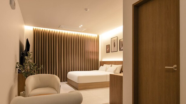 Un dormitorio moderno con cama, una silla, una mesita de noche y una puerta de madera.