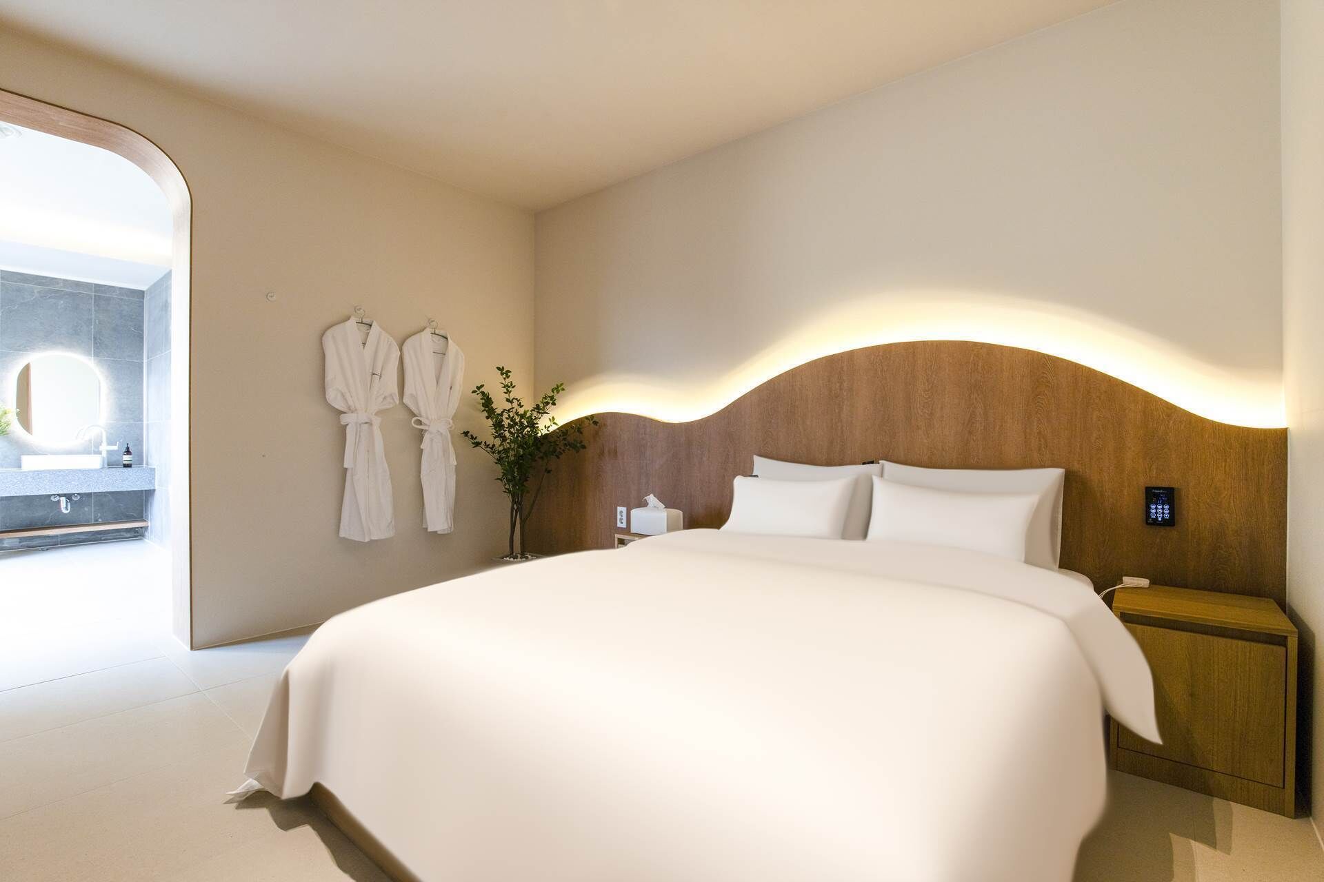 Een hotelkamer met een groot bed, een houten hoofdbord, een nachtkastje en een bedieningspaneel aan de muur.