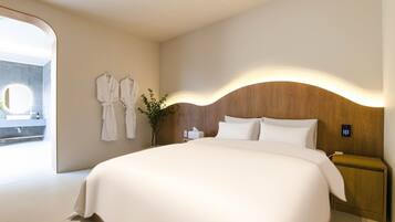 Een hotelkamer met een groot bed, een houten hoofdbord, een nachtkastje en een bedieningspaneel aan de muur.