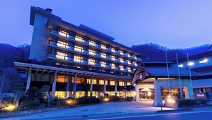 A multi-story hotel with a traditional Japanese architectural style, featuring a large entrance with a covered walkway and a stone building adjacent to it. - Ooedo Onsen Monogatari Premium Sendai Sakunami (Sendai)