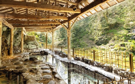 A traditional Japanese onsen with wooden beams, stone steps, and a bamboo fence.