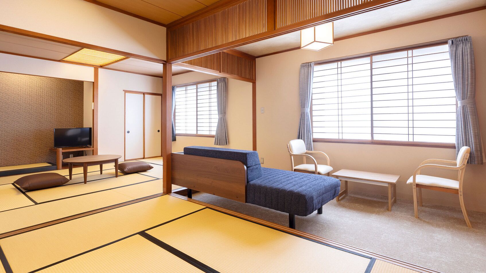 Una habitació japonesa tradicional amb paviment de tatami, un llit de futó, una televisió, un escriptori i una cadira.