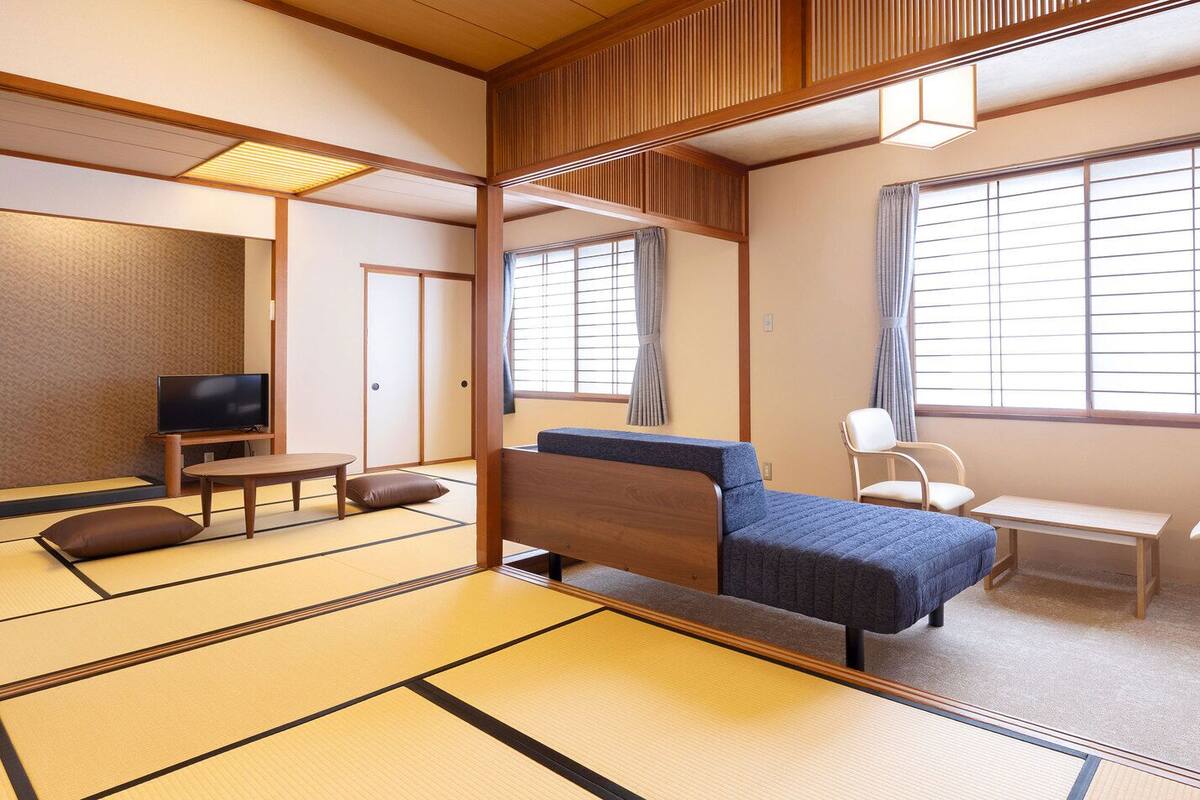 Une pièce de style japonais traditionnel, avec un sol recouvert de tatamis, un futon servant de lit, une télévision, un bureau et une chaise.