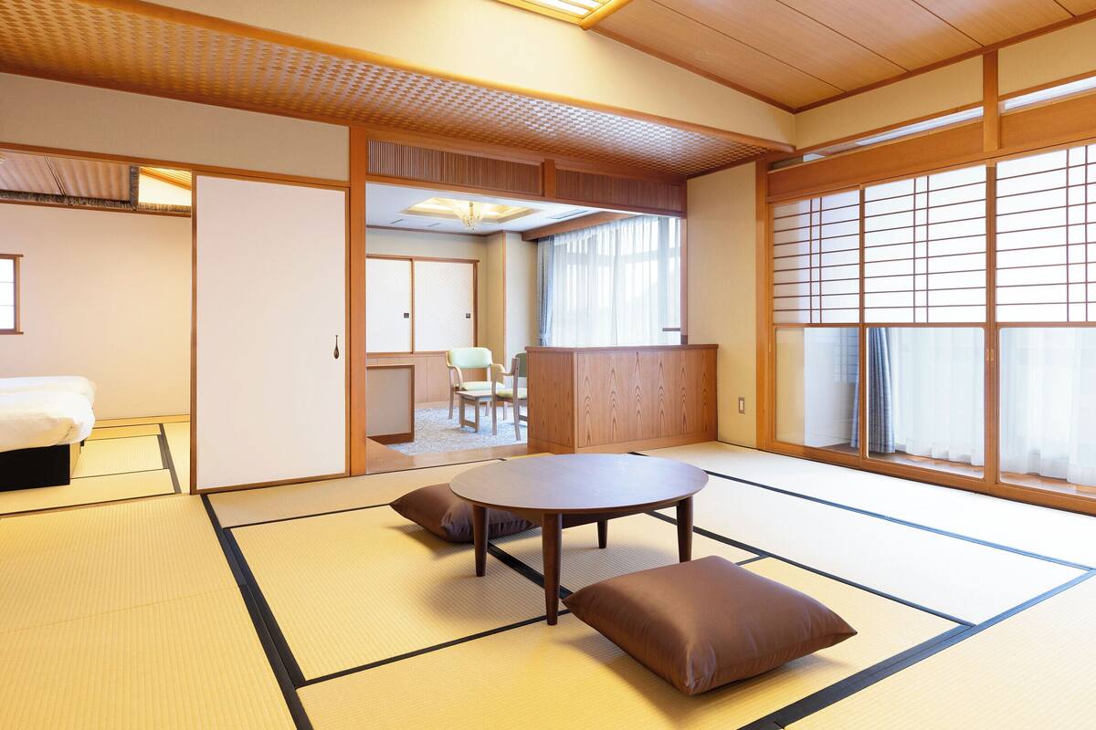 A traditional Japanese room with tatami flooring, a low table with cushions, sliding doors, and a view through a shoji screen.