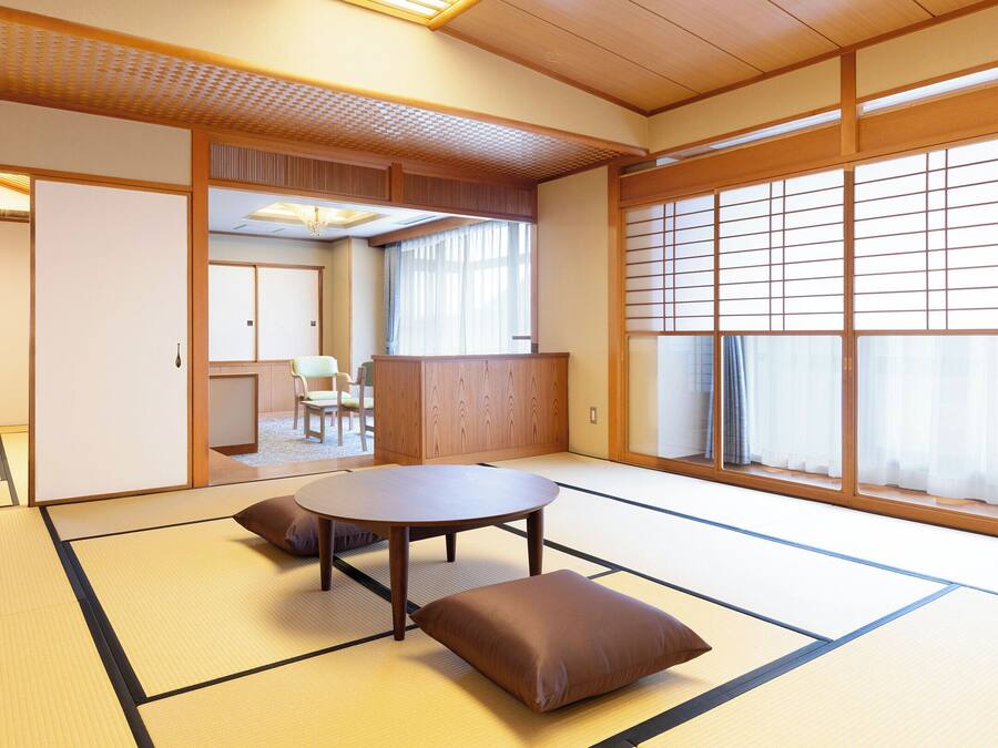 Una habitación japonesa tradicional con suelo de tatami, una mesa baja con cojines, puertas correderas y vistas a través de un celosía shoji.