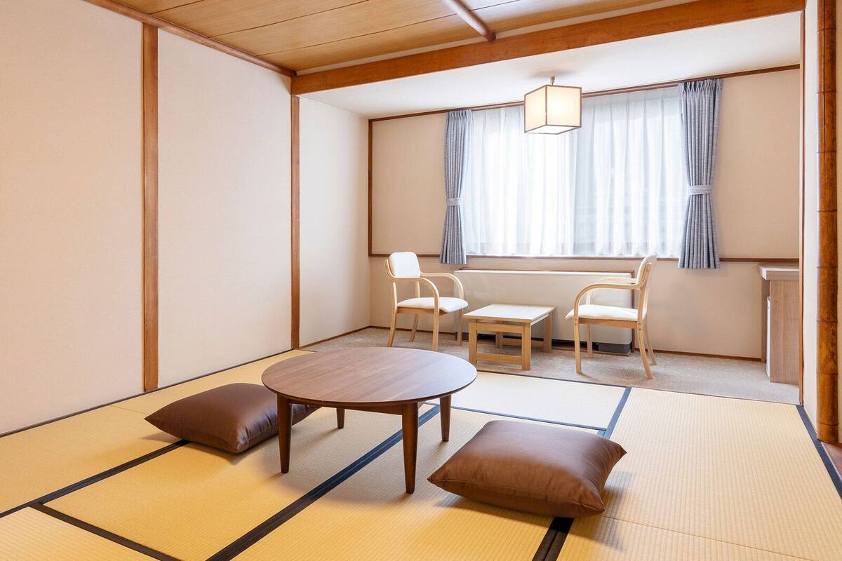 A tatami mat room with a low table, two chairs, and a pillow.