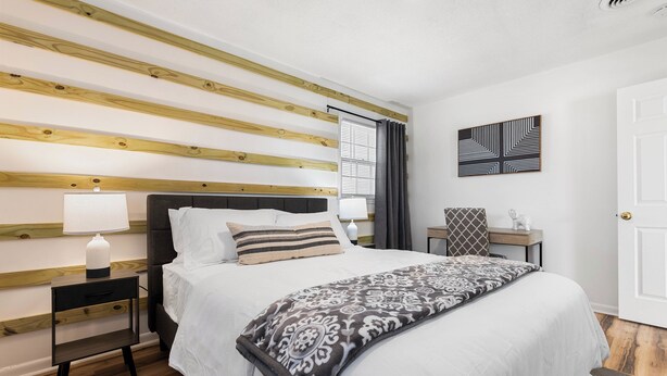 Un dormitorio ordenado con cama, mesitas de noche, lámpara y una obra de arte colgada en la pared.